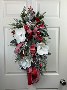 a christmas wreath hanging on the front door with red and white flowers, greenery and berries