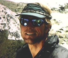 a man wearing sunglasses and a hat standing in front of rocks with snow on them