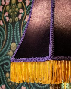 a purple lamp with gold fringes on it and a floral wallpaper behind it