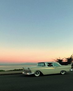 an old car is driving down the road by the ocean at sunset or sunrise time