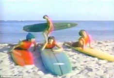 four people sitting on surfboards in the sand with one person holding a surfboard