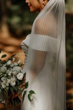 a woman wearing a veil holding a bouquet of flowers in her hand and looking off to the side