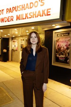 a woman standing in front of a movie theater with her hands in her pockets and looking at the camera