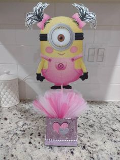 a pink and yellow cake with a minion on it's head sitting on top of a box