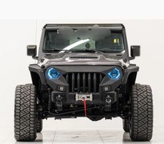 the front end of a black jeep with its lights on and four wheels parked in a white room