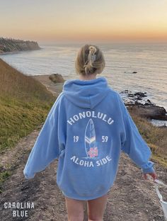 a woman walking down a dirt road next to the ocean