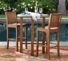 two wooden chairs sitting at a table in front of a pool with flowers on it