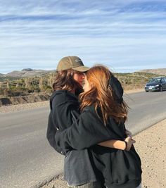 two people hugging each other on the side of the road with a car in the background