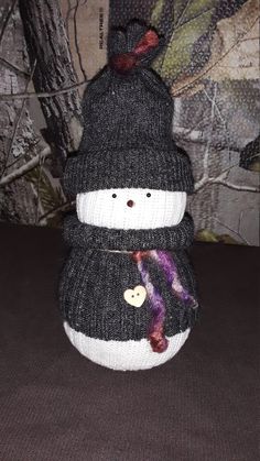 a knitted snowman sitting on top of a table next to a tree trunk