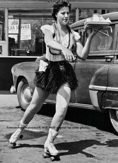 an old photo of a woman rollerblading in front of a car and holding a skateboard