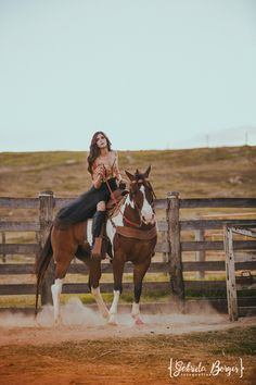 a woman riding on the back of a brown and white horse next to a wooden fence