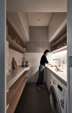 a woman standing in a kitchen next to a washer and dryer with shelving on the wall