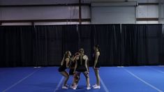 three girls in black and white uniforms standing on a blue floor with their arms around each other