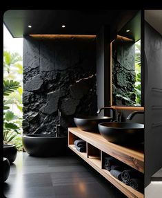 two pictures of a bathroom with black walls and flooring, one has a large stone wall