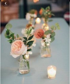 several vases with flowers and candles on a blue table cloth covered table in an indoor setting