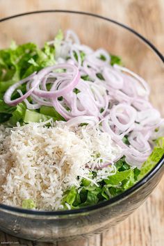 a salad with onions and lettuce in a glass bowl on a wooden table