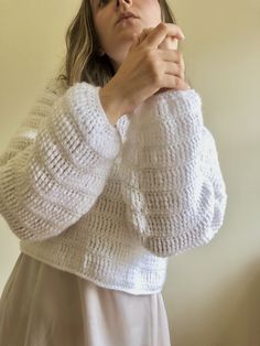 a woman in a white sweater is holding her hands on her chest and looking at the camera