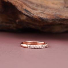 a rose gold wedding band with five diamonds on the side, sitting next to a rock