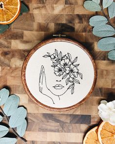 an embroidery project with oranges and leaves on the table next to it is a drawing of a woman's face