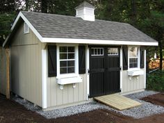 a small shed with two windows and a door on the side, in front of some trees