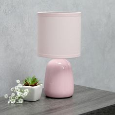 a pink table lamp next to a small potted plant on top of a wooden table