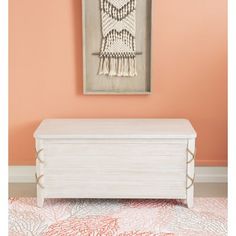 a white chest with tassels on top in front of an orange wall and pink rug