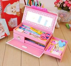 an open pink children's jewelry box sitting on top of a wooden table next to other items