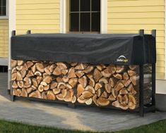 a large pile of logs sitting in front of a yellow house with a black cover over it