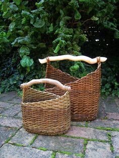 two wicker baskets sitting next to each other on a stone floor in front of bushes