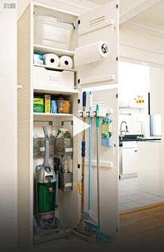 the inside of a white cabinet filled with cleaning supplies and tools, including a mop