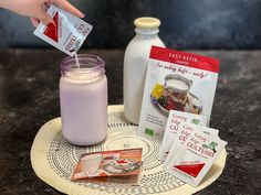 a hand is pouring milk into a glass jar on a plate with other items around it