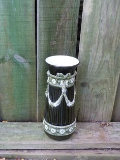 a black and white vase sitting on top of a wooden bench next to a fence