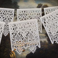 three white crochet doily hanging on a string in front of a painting