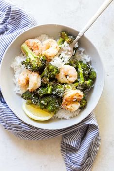 a white bowl filled with shrimp and broccoli on top of rice next to a blue towel