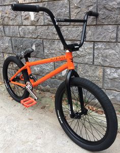 an orange bike parked next to a brick wall