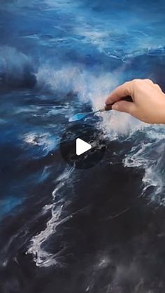 a person is holding something in their hand over the ocean with blue water and white foam