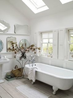 a white bath tub sitting next to a sink under two mirrors and a mirror on the wall