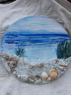 a painted plate with seashells and shells on the sand by the water's edge