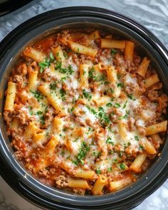 a crock pot filled with pasta and meat covered in sauce, cheese and parsley