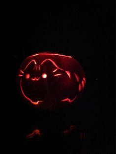 a pumpkin carved to look like a cat with eyes glowing in the dark, lit up at night