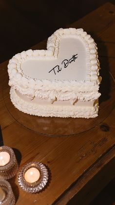 a heart shaped cake sitting on top of a wooden table next to two tea lights