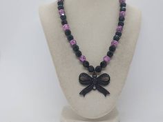 "Bow Necklace - Black Bow Necklace - Pink and Black Necklace - Gothic Necklace - Pink and Black Necklace For Women - Bow Necklace For Women This necklace measures 17 1/2\" in length.  This necklace is comprised of a black metal black jeweled bow pendant, pink acrylic beads with black swirls of color on them, and black acrylic multifaceted beads.  This necklace is strung on beading wire with a lobster clasp for closure.  So I found the black bow pendant and I fell in love with it.  The black jewels on it give it a great sparkle.  So to compliment the bow I used pink and black beads.  This necklace has a Gothic look.  This necklace is great for concerts and music events!" Black Beaded Necklace For Gift, Black Necklace With Ribbon For Gift, Adjustable Black Necklace With Black Ribbon, Black Ribbon Jewelry For Gift, Purple Necklace With Black Beads For Gift, Gift Purple Necklace With Black Beads, Black Jewelry With Black Ribbon For Party, Adjustable Purple Necklace With Black Beads, Bow Pendant