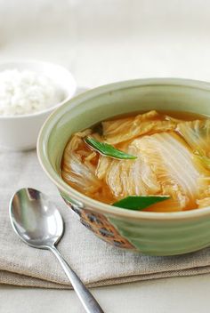 a green bowl filled with soup next to two spoons and a cup of rice