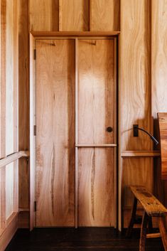 an empty room with wood paneling and wooden bench in front of the door that leads to another room