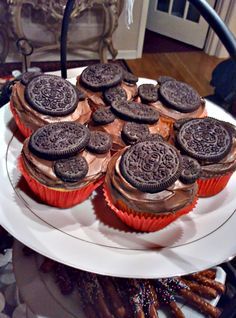 chocolate cupcakes with oreo cookies are on a white plate next to some pretzels