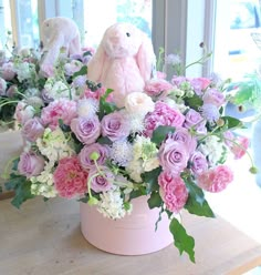 a pink vase filled with lots of flowers on top of a wooden table next to a window