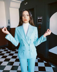 a woman in a blue suit standing on a checkered floor with her hands out