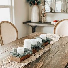 candles are arranged on a wooden table in front of a vase with greenery and pine cones