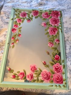 a mirror with flowers painted on it sitting on top of a bed next to a person's feet