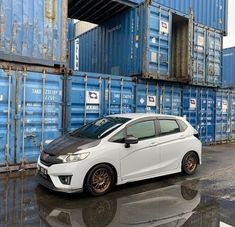 a white car is parked in front of some shipping containers